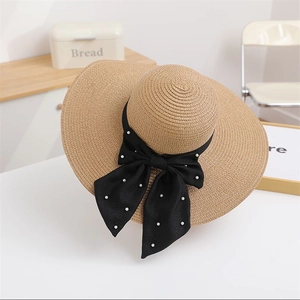 Detail of a straw sun hat with a wide brim featuring a black ribbon and white pearl bow