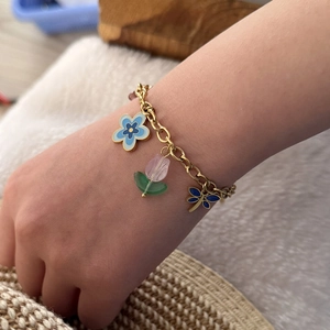 Close-up of gold chain bracelet with blue flower, tulip and dragonfly charms on wrist