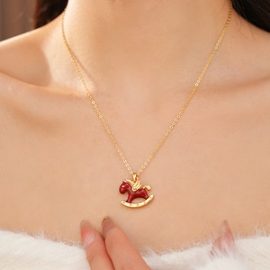 Close-up of golden necklace with a red enamel rocking horse pendant on a model neck