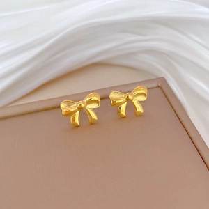 Macro shot of gold bow stud earrings on brown stand with elegant silk background