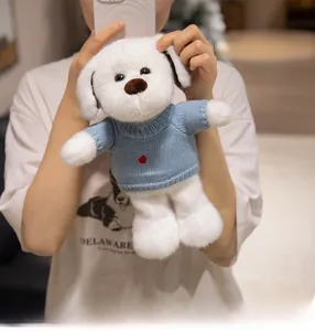 Gros plan d'un chien en peluche blanc portant un pull en tricot bleu avec cœur et rose brodés