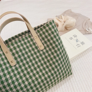 Detail of green and white plaid tote bag with faux leather handle and gold metal rivets