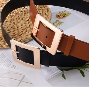 Detail shot of black and brown wide belts with square gold buckles on a lifestyle background