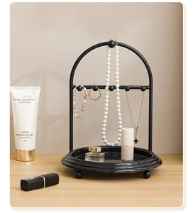 Modern black arched metal jewelry organizer stand on a wooden desk with a storage tray