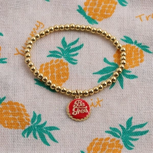 Goldene Perlenarmband mit rotem Kronkorken-Anhänger und Be Free-Schriftzug für Damen