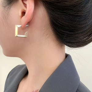 Close-up of a minimalist gold square geometric earring on model with brushed metal finish