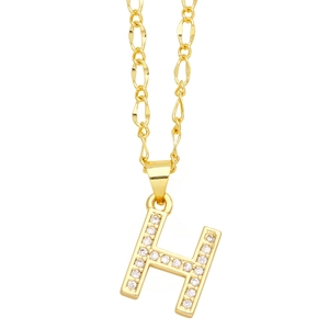 Macro detail of gold Figaro chain and capital letter H pendant with micro-set zircons