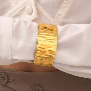 Detail of wide gold layered cuff bracelet with irregular wrinkled texture on a model wrist