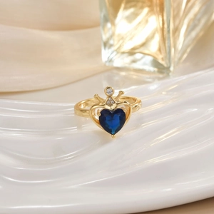 Macro view of golden heart ring with blue gemstone and crown detail on white tray