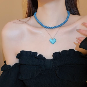 Close-up of double layer necklace featuring blue beads and transparent heart pendant