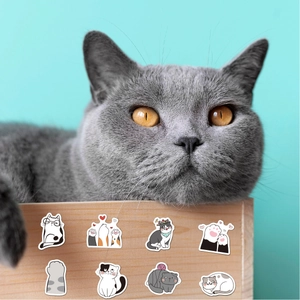 Close-up of cute cartoon cat and paw stickers applied on a wooden box near a gray cat
