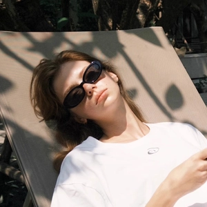 Close-up of retro oval sunglasses with black frames worn by a model in outdoor sunlight