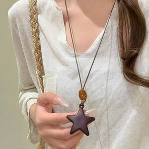 Detail of star pendant necklace with amber bead on brown cord worn by a model