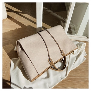 Detail of beige canvas tote bag with brown leather trim and metal chain strap