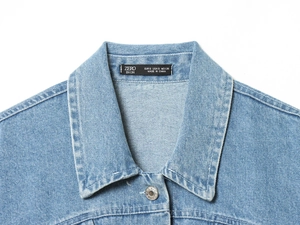 Nahaufnahme der hellblauen Jeansjacke mit Metallknöpfen und aufgenähtem Markenetikett
