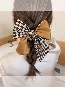 Back view of a large houndstooth and caramel satin bow hair clip on a low ponytail