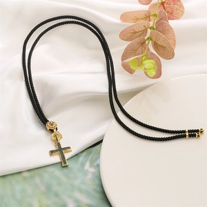 Close-up of gold cross pendant with green stones on black cord and white silk background