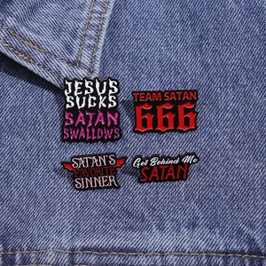 Vue détaillée de quatre pin's en émail noir avec texte gras posés sur un tissu denim bleu