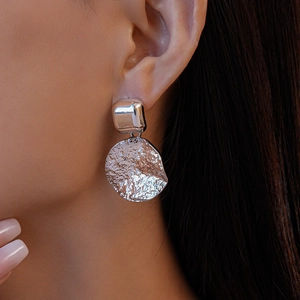 Gros plan de boucle d'oreille géométrique argentée texturée portée sur modèle