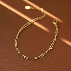 Macro shot of double-layered gold-plated square charm bracelet on brown leather