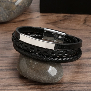 Detail of multilayer black leather woven bracelet with silver metal bar on a stone base