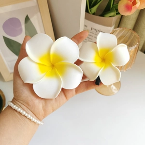 Detailed close-up of realistic white and yellow frangipani flower hair clips in two sizes