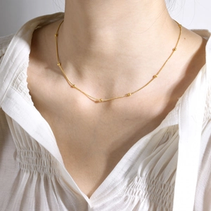 Macro view of gold beaded chain necklace showing minimalist texture on female neck