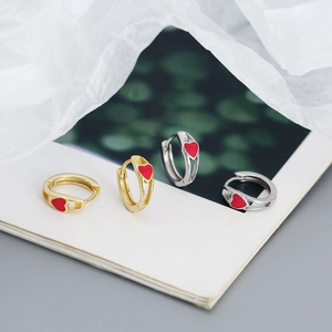 Detail of gold and silver S925 earrings with red enamel hearts on open book pages