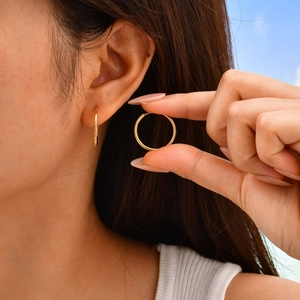 Detail view of thin gold stainless steel hoop earrings held by hand and worn for size