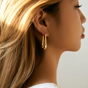 Close-up of minimalist U-shaped 18K gold plated earring worn by a model in soft light
