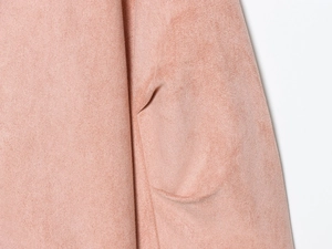 Detailopname van de suède textuur en zakstiksels op de roze jas met opstaande kraag