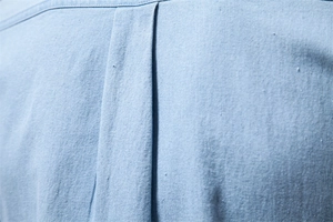 Close-up of light blue denim shirt fabric showing back pleat and cotton texture
