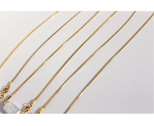 Detailed view of gold snake chains with a square baroque pearl pendant on white background