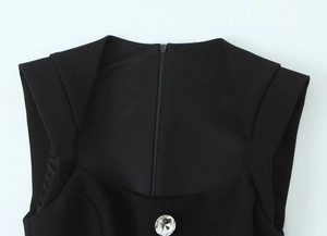 Detail of black garment featuring a central zipper and a large sparkling rhinestone button