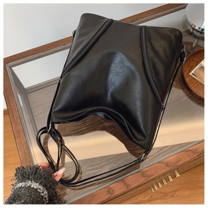 Detail of minimalist black PU leather shoulder bag featuring dual diagonal zippers