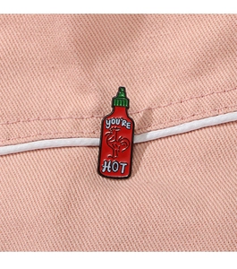Close-up of Sriracha sauce bottle enamel pin on pink denim with YOU'RE HOT text
