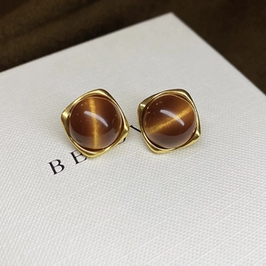 Macro shot of gold earrings featuring round brown tiger eye stones in a textured gift box