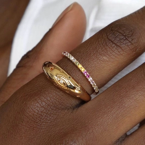 Detail of stacked 18k gold plated evil eye ring and colorful rainbow zircon band on finger