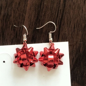 Detail of red Christmas gift bow earrings on white card display over dark wood surface