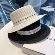 Detail view of black and white wide-brim straw hats with ribbon and golden M metal accessory