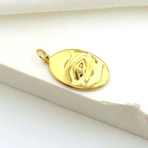 Close-up of a gold oval pendant featuring an engraved eye motif on a white fabric surface