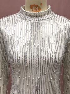 Detalle de vestido blanco con lentejuelas plateadas y flecos con cuello alto refinado