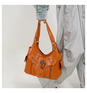 Detail der orangebraunen PU-Ledertasche mit gotischem Metallkreuz und Reißverschlusstaschen