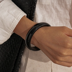 Close-up of a wide polished black resin bangle worn by a model in a retro style