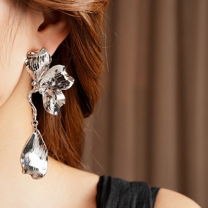 Macro view of silver floral metal earrings with textured petals on a fashion model