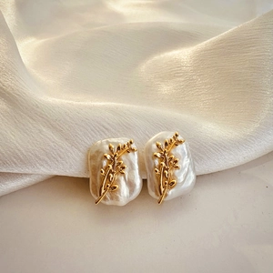 Detailed macro view of baroque pearl earrings with golden olive branch on white silk