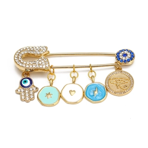 Detail of gold safety pin brooch with Hamsa hand and blue evil eye crystal charms