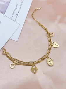 Detailaufnahme des goldenen Charm-Armbands mit Herzschloss, Kreuz und Herzanhängern