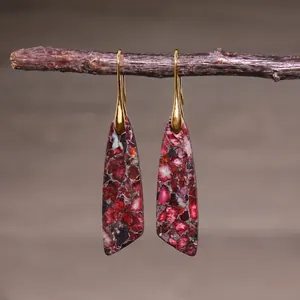 Close-up of teardrop imperial stone earrings hanging on a rustic branch background