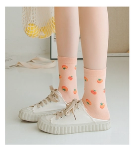 Detail of cotton crew socks in pink featuring orange tomato patterns and white sneakers